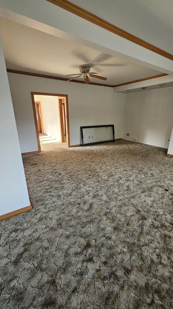 carpeted empty room featuring ornamental molding, baseboards, and a ceiling fan