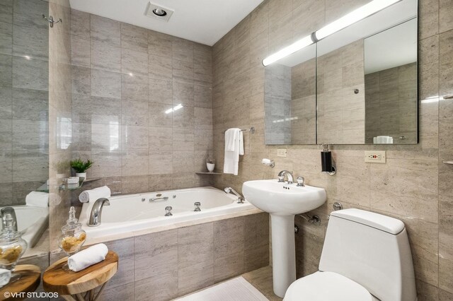 bathroom featuring tiled tub, toilet, and tile walls