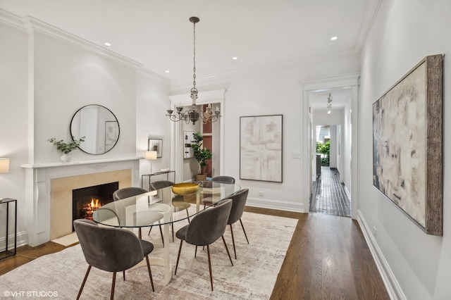 dining room featuring an inviting chandelier, a fireplace, hardwood / wood-style flooring, and ornamental molding