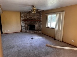 unfurnished living room featuring a fireplace, a textured ceiling, ceiling fan, carpet flooring, and brick wall