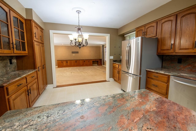 kitchen featuring tasteful backsplash, dark stone counters, stainless steel appliances, pendant lighting, and a chandelier