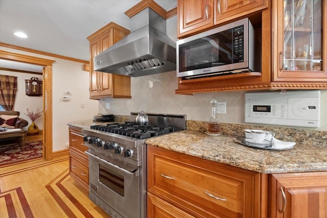 kitchen featuring light wood finished floors, tasteful backsplash, ornamental molding, stainless steel appliances, and exhaust hood