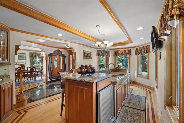 kitchen with beverage cooler, a sink, ornamental molding, brown cabinets, and a tray ceiling