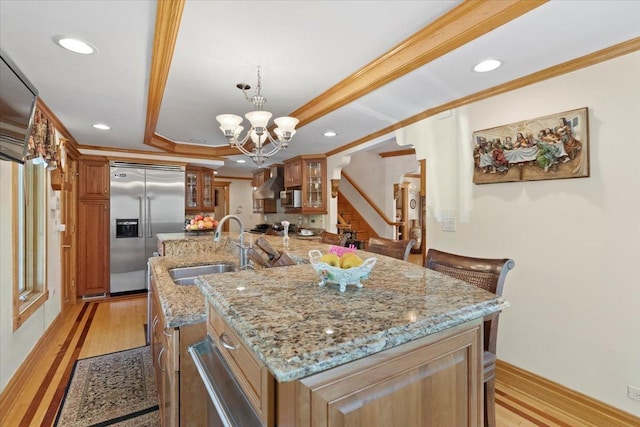 kitchen featuring built in fridge, a sink, ornamental molding, a tray ceiling, and an island with sink