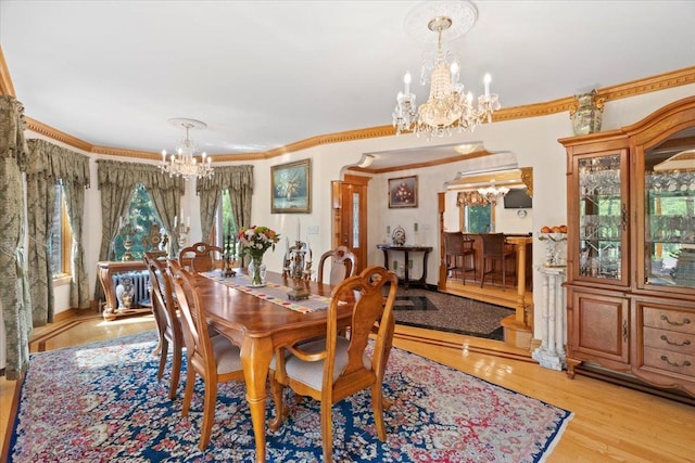 dining space with ornamental molding, light wood-style floors, and an inviting chandelier