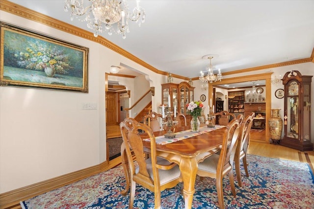 dining area with crown molding, a notable chandelier, light wood-style flooring, and stairs