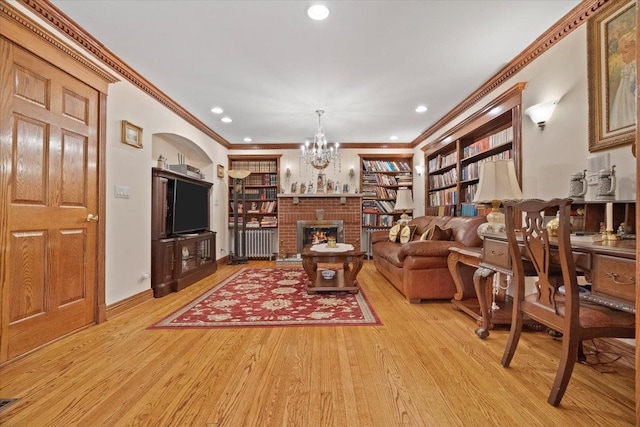 living area with a brick fireplace, ornamental molding, light wood-style floors, and an inviting chandelier