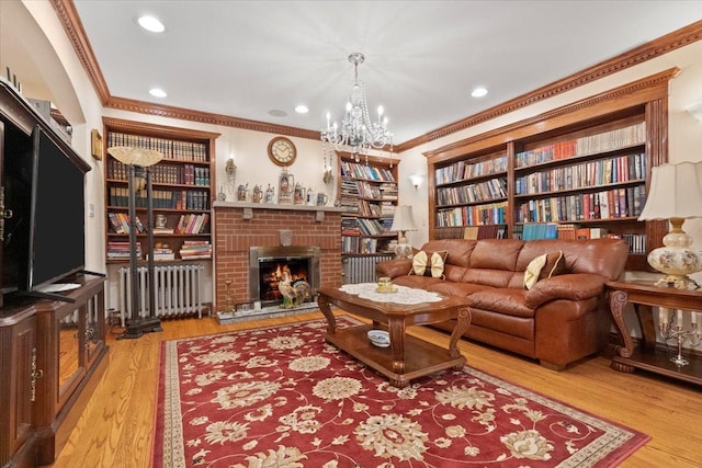 living area featuring a chandelier, a fireplace, wood finished floors, radiator heating unit, and crown molding