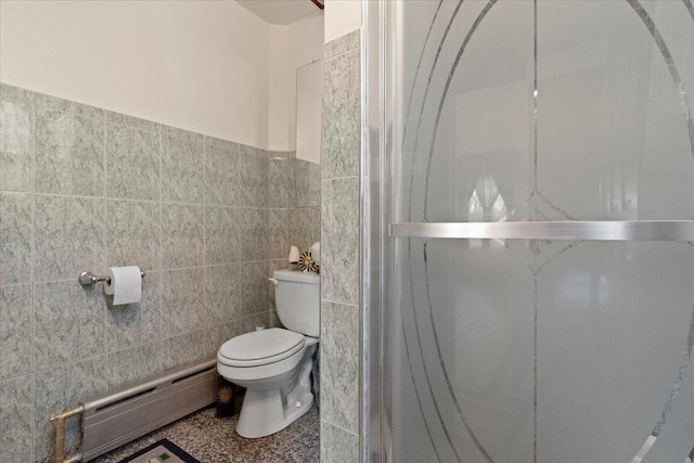 bathroom featuring a shower, toilet, a wainscoted wall, a baseboard heating unit, and tile walls