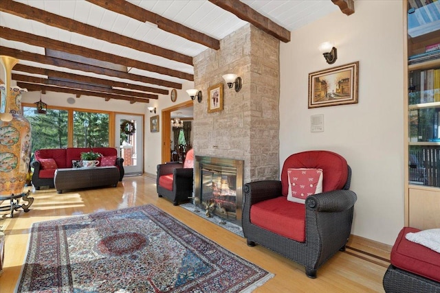 living area featuring beam ceiling, a stone fireplace, and wood finished floors