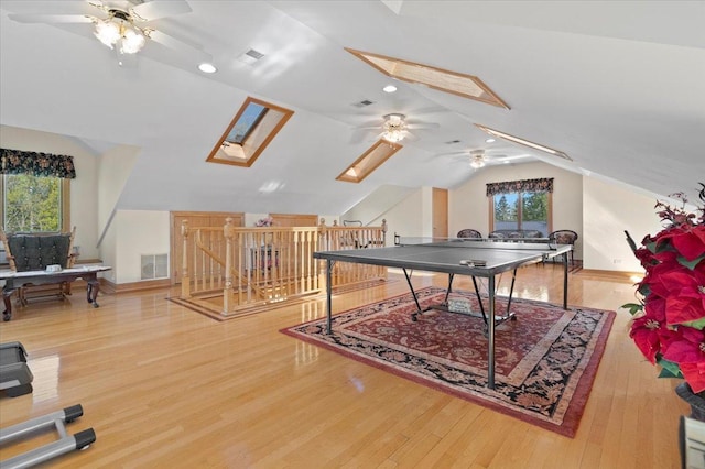 rec room with lofted ceiling with skylight, visible vents, plenty of natural light, and wood finished floors