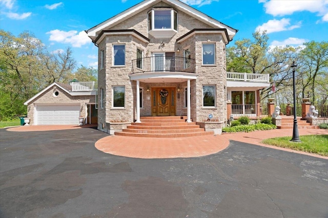 view of front of property with a garage, stone siding, aphalt driveway, and a balcony