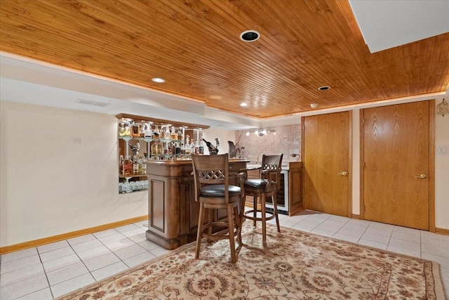 bar featuring a bar, light tile patterned floors, wood ceiling, and baseboards