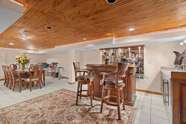 dining space featuring a tray ceiling, light tile patterned floors, a bar, wooden ceiling, and baseboards