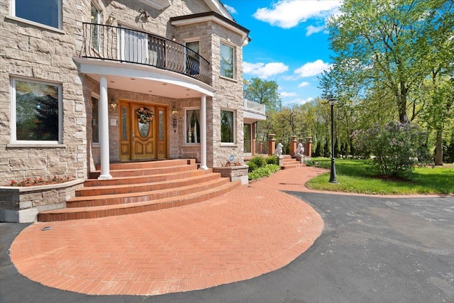 view of exterior entry with stone siding and a balcony