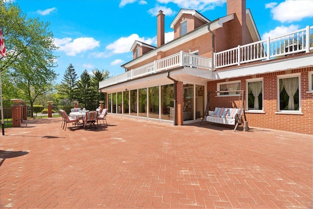 back of house with brick siding, a chimney, a patio area, and a balcony