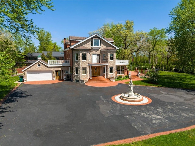 view of front of house featuring aphalt driveway, a chimney, a balcony, a garage, and stone siding