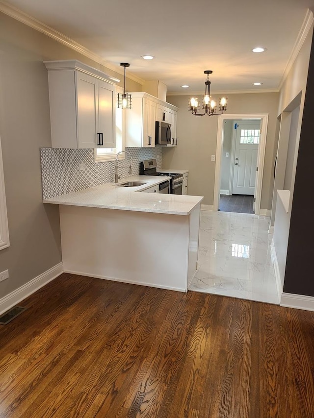 kitchen with kitchen peninsula, appliances with stainless steel finishes, sink, pendant lighting, and white cabinetry