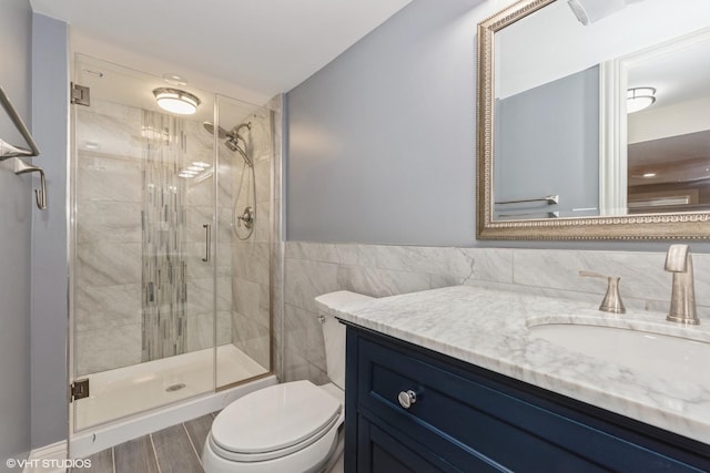 bathroom with vanity, toilet, a shower with shower door, and tile walls