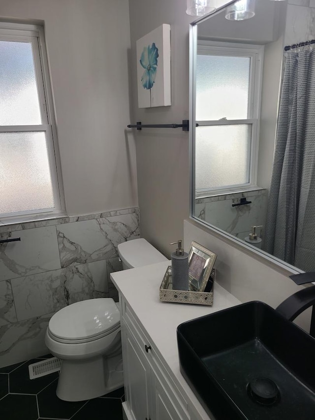 bathroom featuring a shower with curtain, tile patterned flooring, toilet, vanity, and tile walls