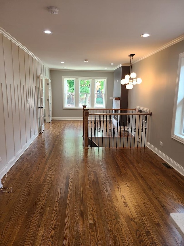 empty room with crown molding, dark hardwood / wood-style floors, and a notable chandelier