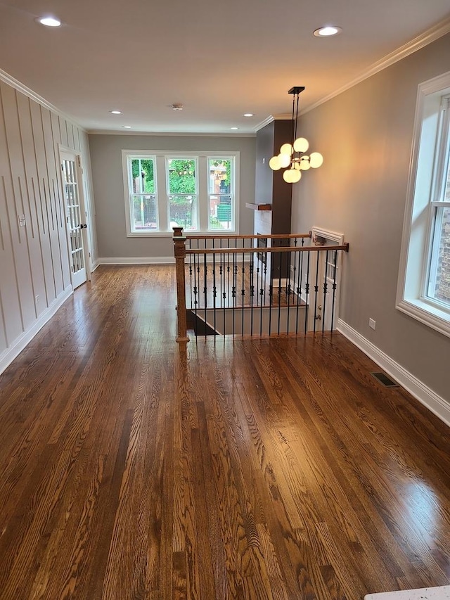 empty room with dark wood-type flooring, ornamental molding, and a notable chandelier