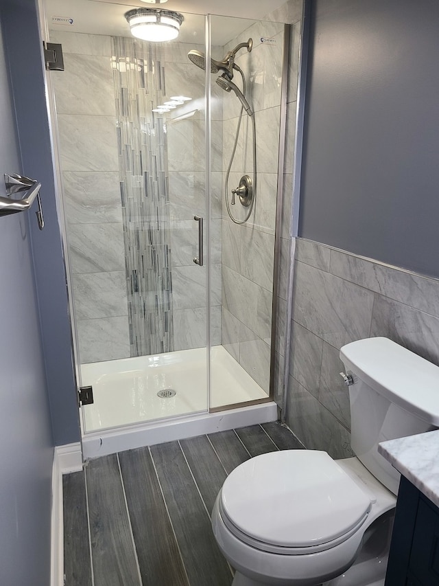 bathroom featuring a shower with door, vanity, tile walls, and toilet