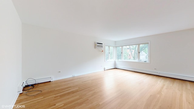 unfurnished room with light wood-style flooring, a baseboard heating unit, baseboards, and a wall mounted air conditioner