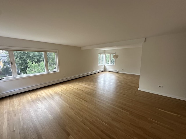 empty room featuring baseboard heating, baseboards, and wood finished floors