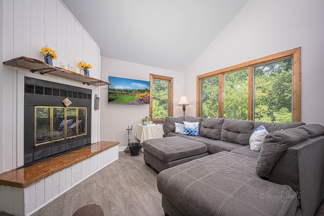 living room with a tile fireplace, light wood-type flooring, and high vaulted ceiling