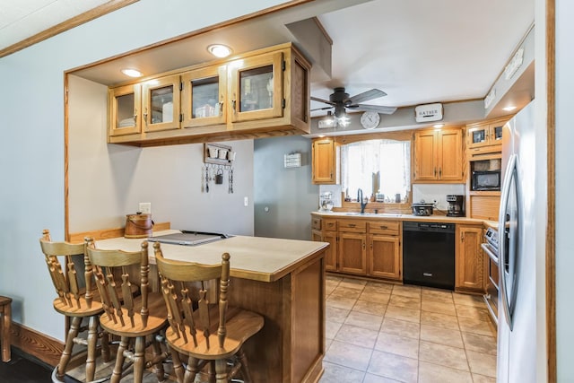 kitchen featuring sink, a breakfast bar area, light tile patterned floors, ceiling fan, and black appliances