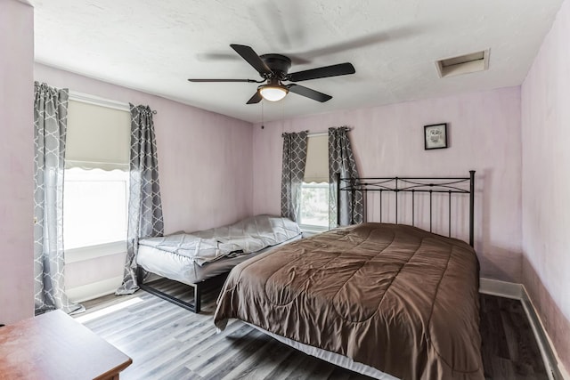 bedroom with multiple windows, a textured ceiling, wood-type flooring, and ceiling fan