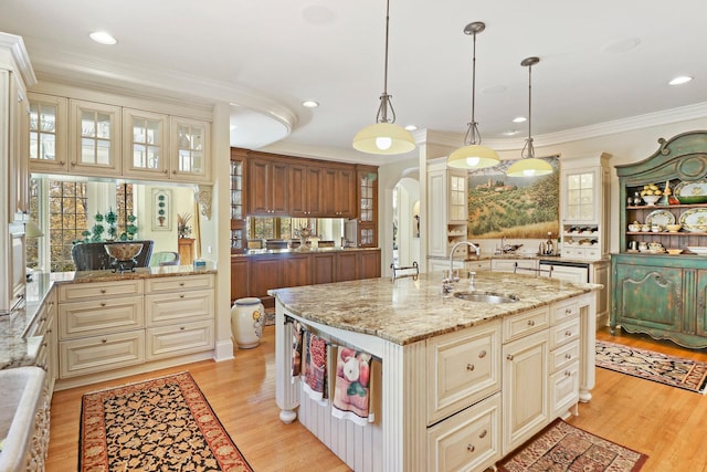 kitchen featuring sink, light stone counters, hanging light fixtures, a center island with sink, and light hardwood / wood-style flooring