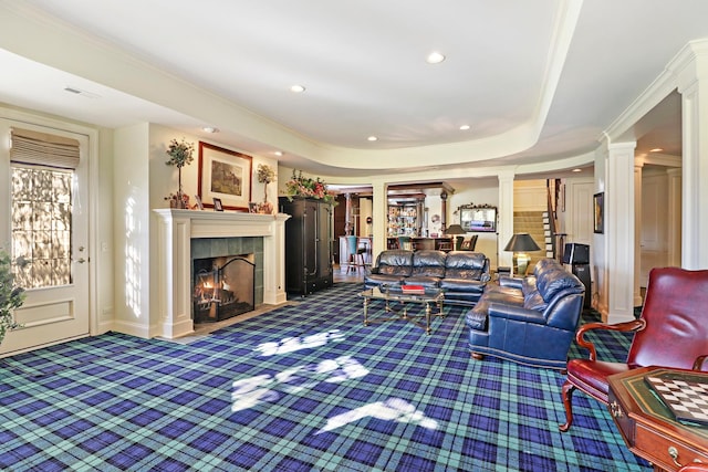 carpeted living room with ornamental molding, a tray ceiling, decorative columns, and a tile fireplace