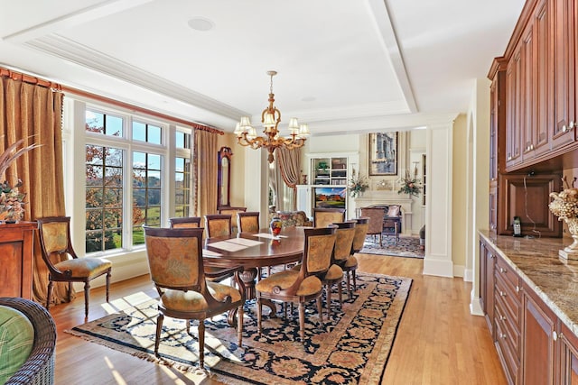 dining space featuring an inviting chandelier, ornamental molding, a tray ceiling, and light hardwood / wood-style floors