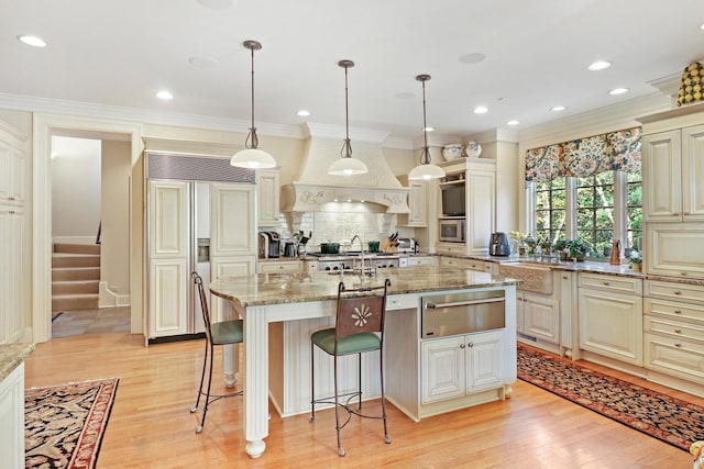 kitchen with pendant lighting, an island with sink, sink, light hardwood / wood-style floors, and light stone countertops