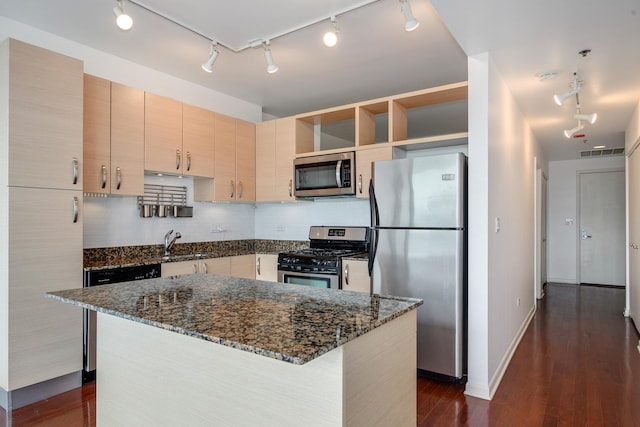 kitchen with appliances with stainless steel finishes, a kitchen island, dark stone countertops, light brown cabinetry, and sink