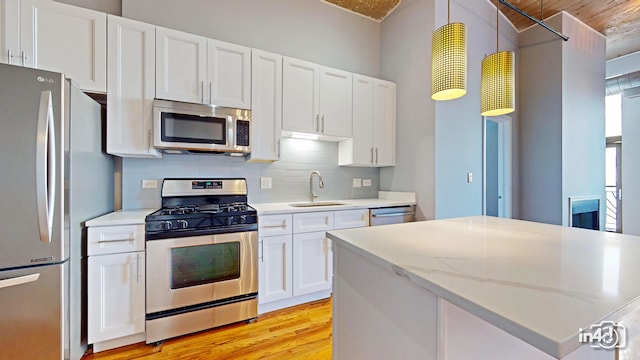 kitchen with light stone counters, light hardwood / wood-style floors, sink, white cabinetry, and appliances with stainless steel finishes