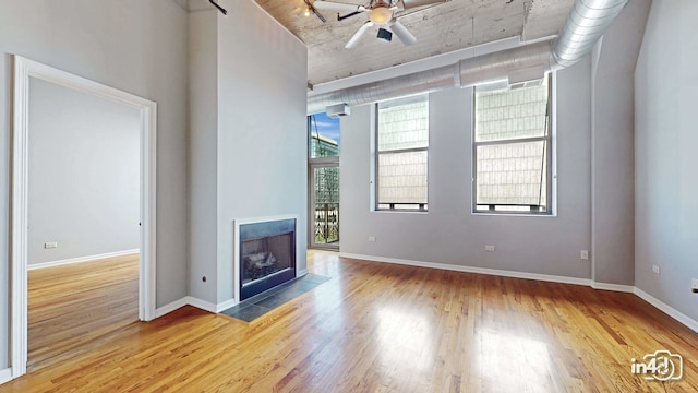 unfurnished living room with ceiling fan, a tiled fireplace, and wood-type flooring