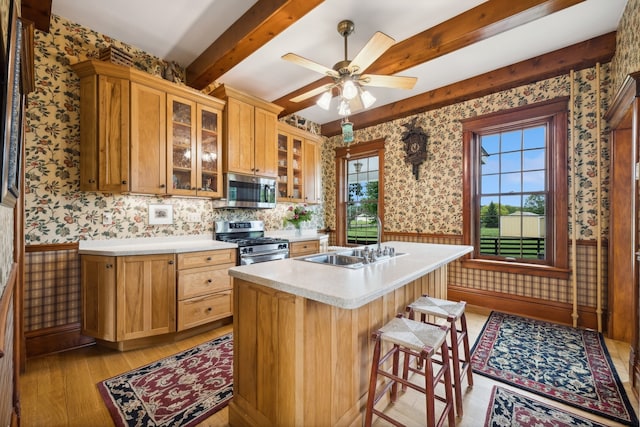 kitchen with ceiling fan, stainless steel appliances, beamed ceiling, light hardwood / wood-style floors, and sink