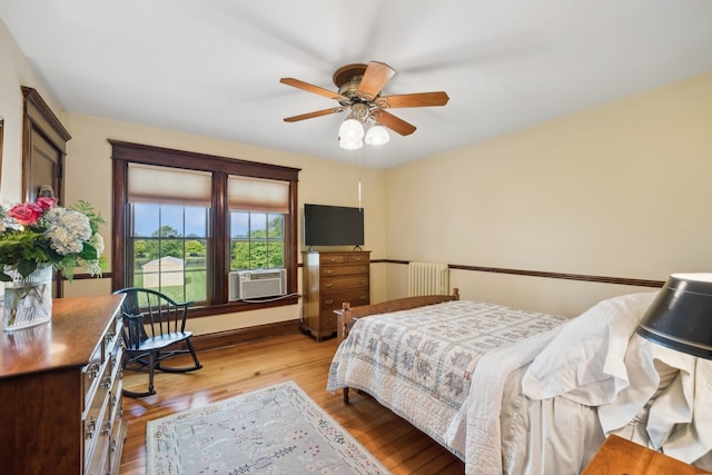 bedroom with cooling unit, radiator, light hardwood / wood-style flooring, and ceiling fan