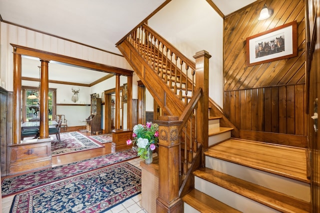 stairs with decorative columns, wood walls, ornamental molding, and tile patterned floors