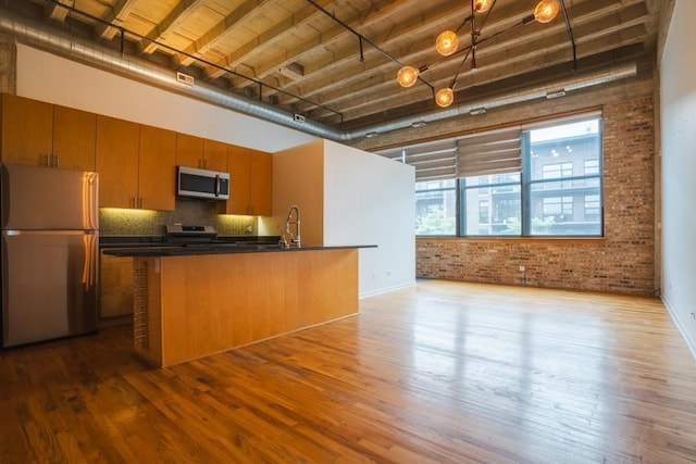 kitchen featuring appliances with stainless steel finishes, light wood-type flooring, a high ceiling, and brick wall