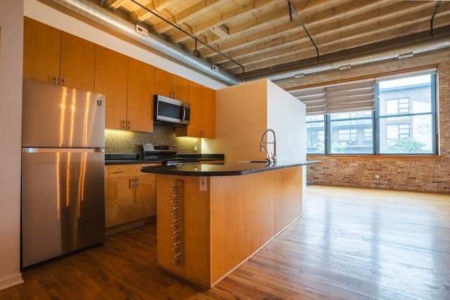 kitchen featuring brick wall, stainless steel appliances, sink, a center island with sink, and hardwood / wood-style floors