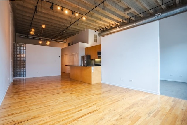 unfurnished living room with track lighting, a high ceiling, and light hardwood / wood-style flooring