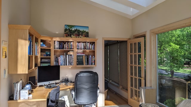 office area featuring wood-type flooring, vaulted ceiling with skylight, and built in desk