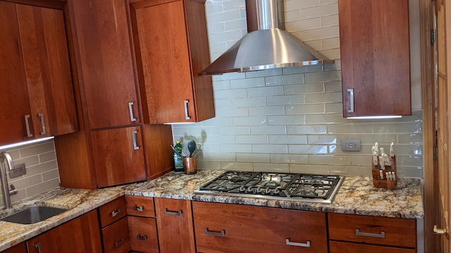 kitchen with stainless steel gas cooktop, wall chimney range hood, sink, light stone counters, and decorative backsplash