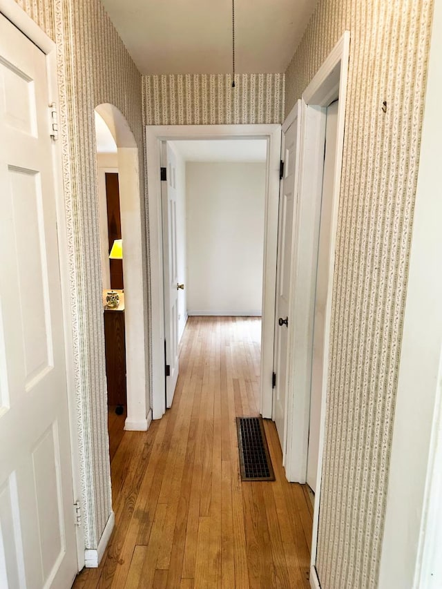 hallway with wallpapered walls, visible vents, light wood finished floors, and arched walkways