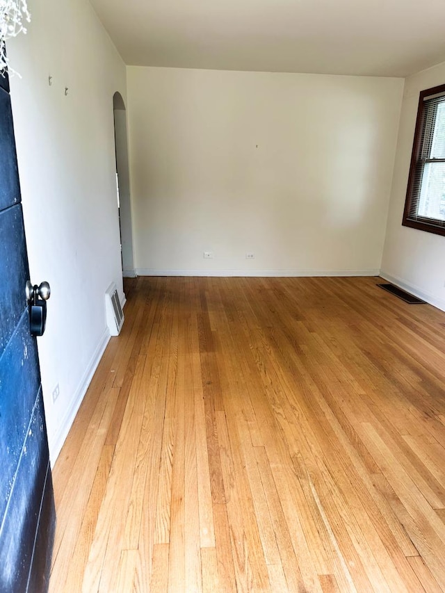 empty room with arched walkways, baseboards, visible vents, and light wood-style floors