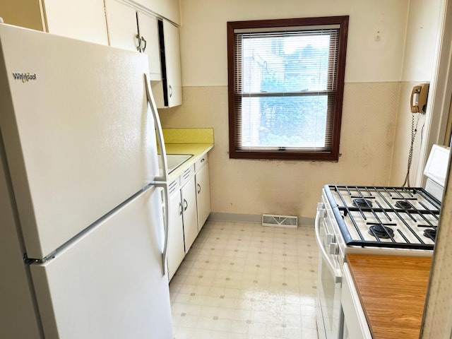 kitchen with a wainscoted wall, light floors, light countertops, visible vents, and white appliances